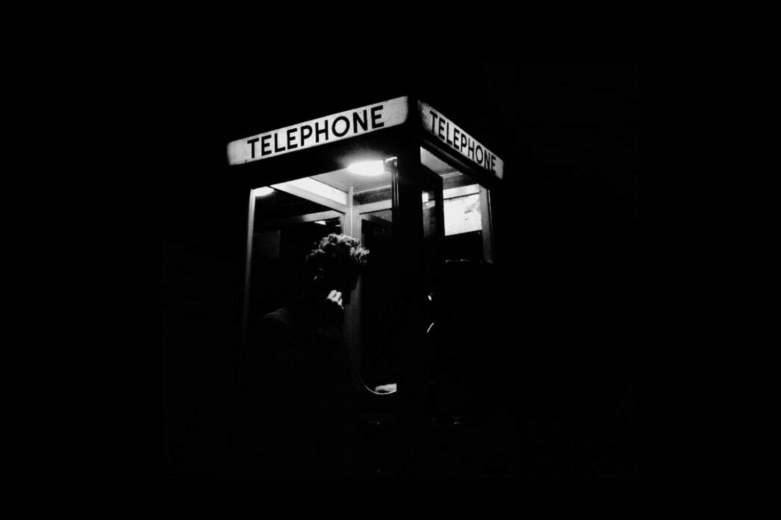 A lit telephone booth at night, figure with receiver